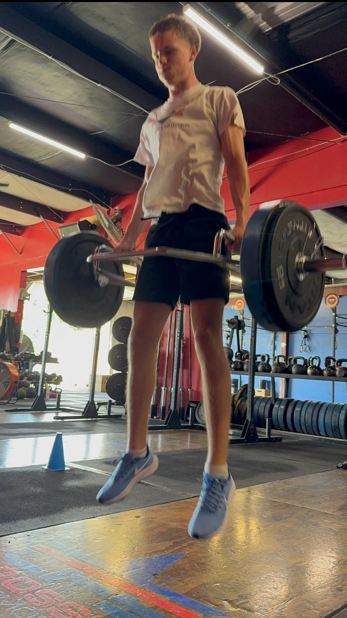 A basketball athlete driving upward out of a trap-bar jump with the bar in his hands
